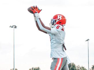 Football player in a white and red uniform catches a pass with arms raised on a field.