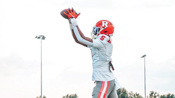 Football player in a white and red uniform catches a pass with arms raised on a field.