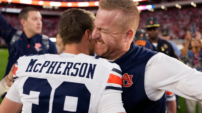 Two football players embrace in a celebratory hug on the field, one wearing a white and navy jersey with 'McPherson' on the back and the other in blue.