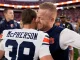 Two football players embrace in a celebratory hug on the field, one wearing a white and navy jersey with 'McPherson' on the back and the other in blue.