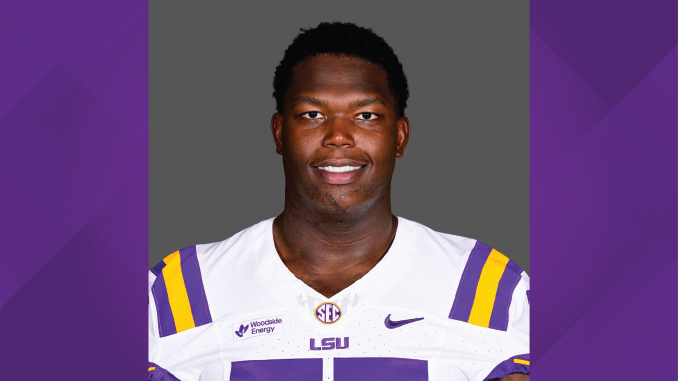 Portrait of an LSU football player wearing a white jersey with purple and gold stripes, against a gray backdrop
