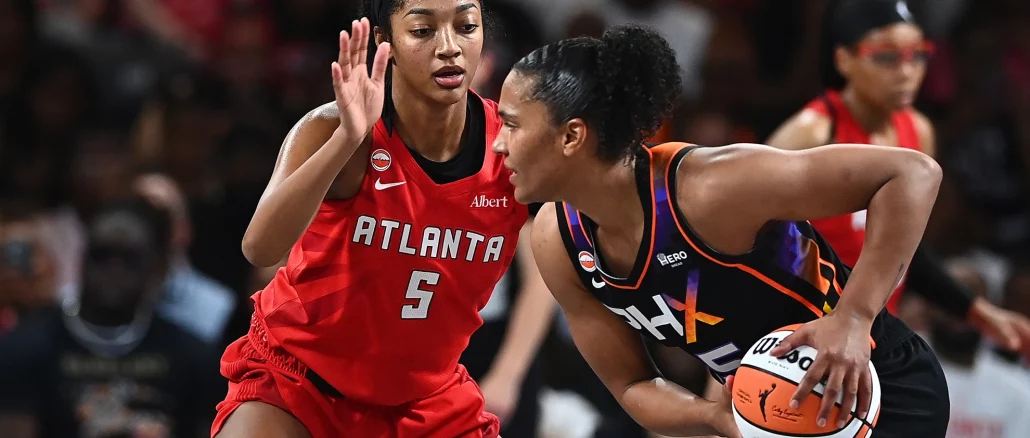 Two female basketball players contesting a loose ball during a game, one in red Atlanta jersey (#5) and the other in black-orange uniform with the ball.