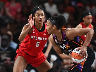 Two female basketball players contesting a loose ball during a game, one in red Atlanta jersey (#5) and the other in black-orange uniform with the ball.