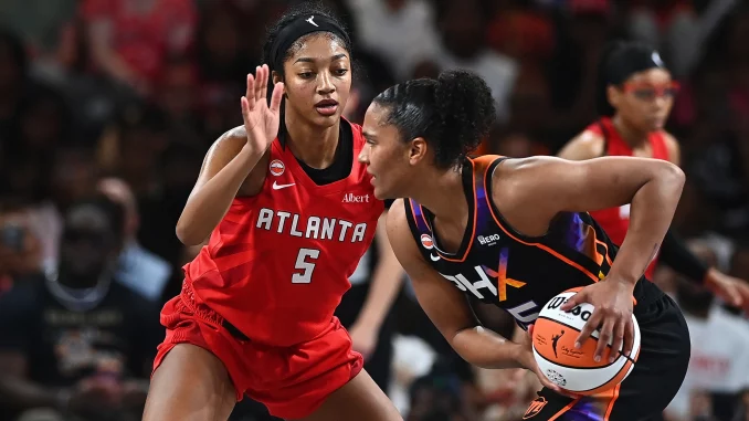 Two female basketball players contesting a loose ball during a game, one in red Atlanta jersey (#5) and the other in black-orange uniform with the ball.