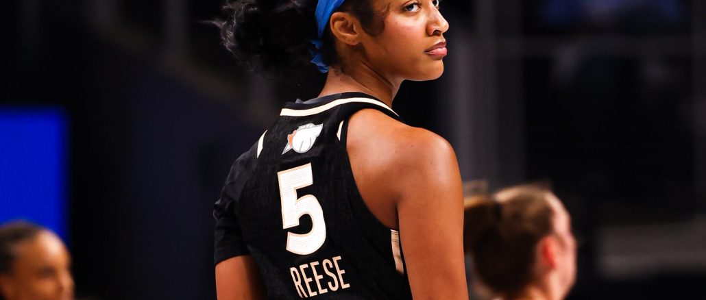 Basketball player wearing a black jersey with the number 5 and a blue headband, looking over her shoulder on the court.