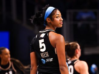 Basketball player wearing a black jersey with the number 5 and a blue headband, looking over her shoulder on the court.