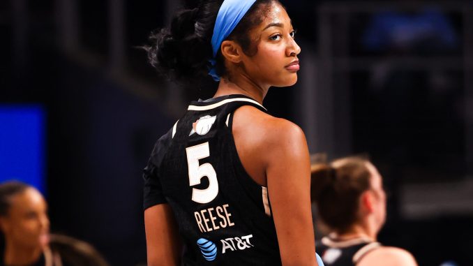 Basketball player wearing a black jersey with the number 5 and a blue headband, looking over her shoulder on the court.