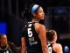 Basketball player wearing a black jersey with the number 5 and a blue headband, looking over her shoulder on the court.