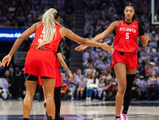 Two Atlanta players in red jerseys high-five on the basketball court during a game, crowd in the stands behind them.