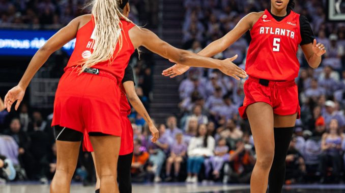 Two Atlanta players in red jerseys high-five on the basketball court during a game, crowd in the stands behind them.