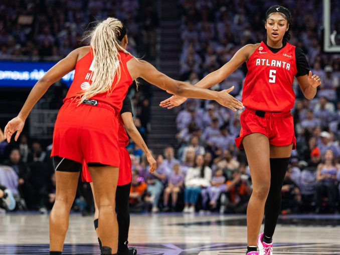 Two Atlanta players in red jerseys high-five on the basketball court during a game, crowd in the stands behind them.