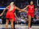 Two Atlanta players in red jerseys high-five on the basketball court during a game, crowd in the stands behind them.