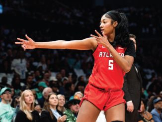 Female basketball player in a red Atlanta jersey No. 5 extends her arm during a game, with a crowded arena in the background.