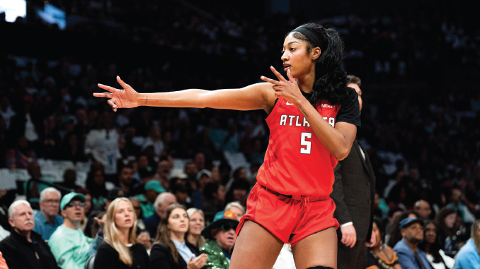 Female basketball player in a red Atlanta jersey No. 5 extends her arm during a game, with a crowded arena in the background.