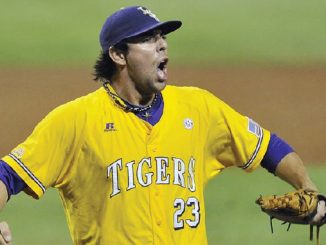 Baseball pitcher in a yellow Tigers jersey (#23) shouting with his glove up, on the mound.