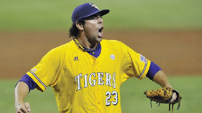 Baseball pitcher in a yellow Tigers jersey (#23) shouting with his glove up, on the mound.