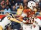 Texas Longhorns player carrying the football and dodging a tackle from a defender in navy and gold inside a crowded stadium