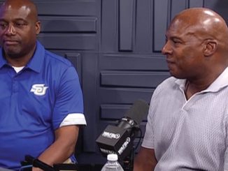 Two men sit at a podcast table with microphones; one in a blue polo, the other in a light gray polo, speaking to the camera side by side.
