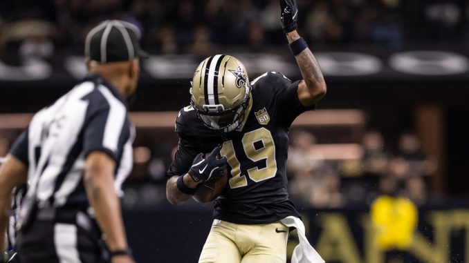 New Orleans Saints player in black and gold celebrates with his right arm raised on the field, an official nearby in view.
