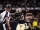 New Orleans Saints player in black and gold celebrates with his right arm raised on the field, an official nearby in view.