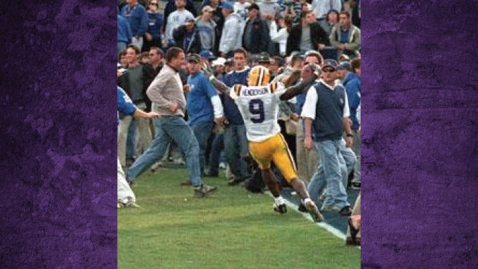 American football player in a white and yellow uniform with number 9 celebrates near the sideline as fans and bystanders crowd the field.