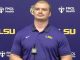 LSU athlete in a purple polo speaks at a press conference with a microphone in front and FMOL Health/LSU backdrop.