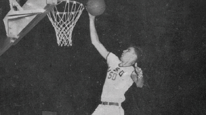 Black-and-white photo of a basketball player leaping to dunk the ball, reaching toward the hoop with the ball in hand, wearing a jersey with number 50