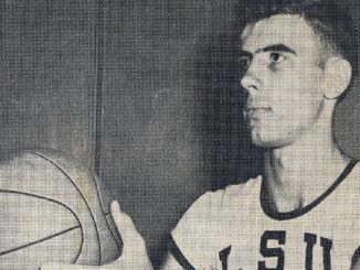 Young man in a USA basketball jersey holding a basketball and looking to the right.