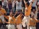 Baseball players in yellow jerseys celebrate with raised arms in a stadium, fans cheering in the background.