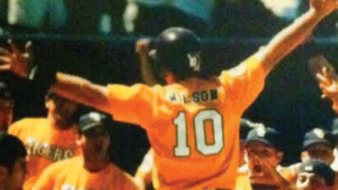 Baseball player in an orange jersey with number 10 raises arms in celebration as teammates cheer nearby.