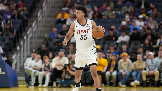 Basketball player in a white Heat jersey with number 55 dribbles the ball on court, focused during a game with spectators in the stands.