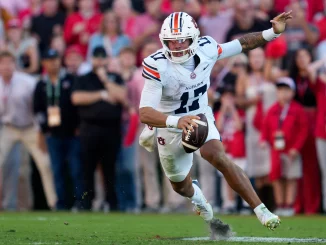 Auburn football player wearing number 11 in a white jersey runs with the ball on the field, crowd in the blurred stands behind him.