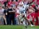 Auburn football player wearing number 11 in a white jersey runs with the ball on the field, crowd in the blurred stands behind him.