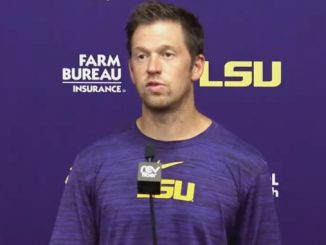 Man in a purple LSU shirt speaks at a press conference with LSU and Farm Bureau logos in the background