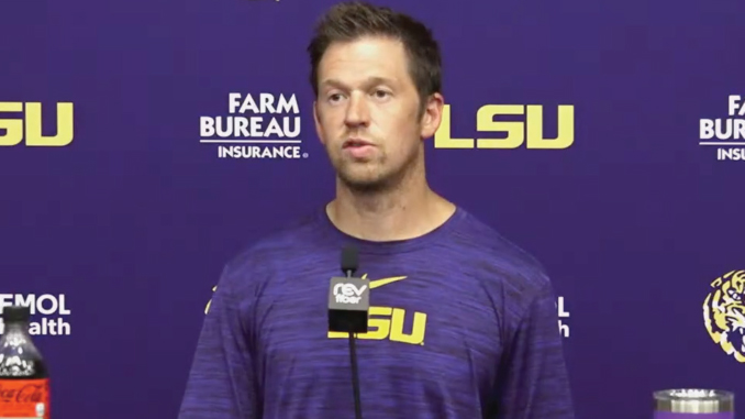 Man in a purple LSU shirt speaks at a press conference with LSU and Farm Bureau logos in the background
