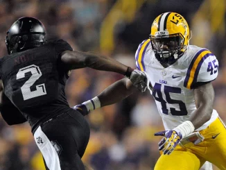 LSU defender #45 in white and gold reaches to tackle an opposing player in a black uniform during a football game.