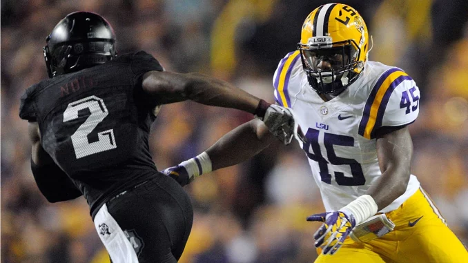 LSU defender #45 in white and gold reaches to tackle an opposing player in a black uniform during a football game.
