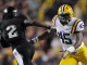 LSU defender #45 in white and gold reaches to tackle an opposing player in a black uniform during a football game.