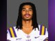 LSU football player with braided hair wearing a white jersey with purple and gold stripes, facing the camera.