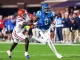 Ole Miss running back in blue carries the ball as a Florida defender in white chases him on a green field.