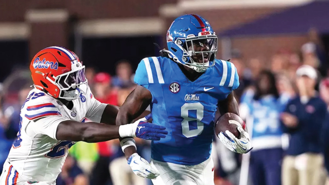 Ole Miss Rebels player in blue jersey carries the football, pursued by a Florida Gators defender in white.