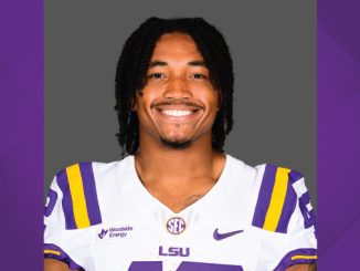 Portrait of a smiling LSU football player in a white jersey with purple and gold stripes, standing against a purple background.
