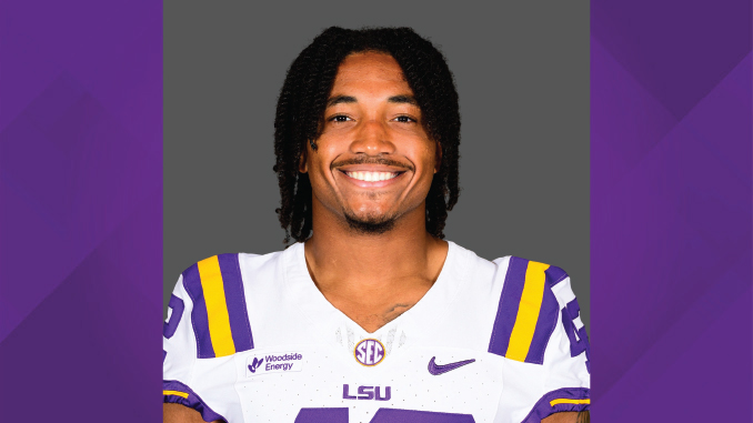 Portrait of a smiling LSU football player in a white jersey with purple and gold stripes, standing against a purple background.