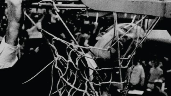 Close-up of a worn basketball net with players and spectators visible in the background.