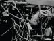 Close-up of a worn basketball net with players and spectators visible in the background.