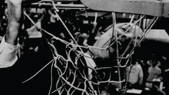 Close-up of a worn basketball net with players and spectators visible in the background.