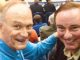 Two smiling men pose for a photo at what looks like a crowded event or gathering.
