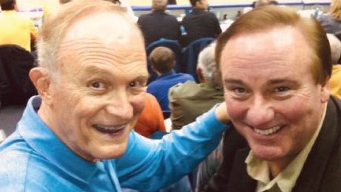 Two smiling men pose for a photo at what looks like a crowded event or gathering.