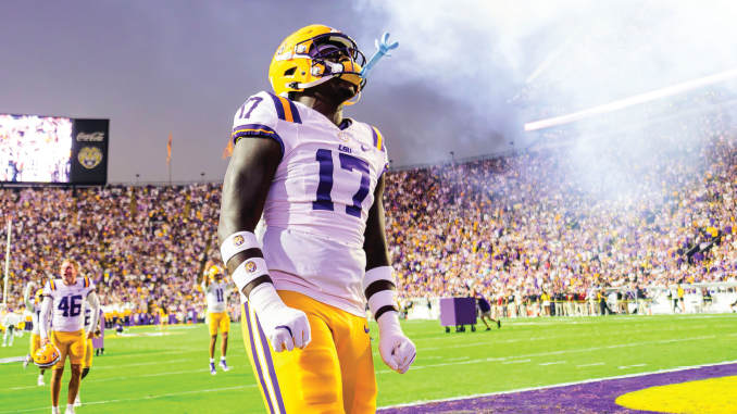 LSU football player wearing number 17 badge stands on the field amid a cheering stadium and smoke from pyrotechnics in the background.
