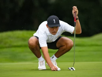 Golfer in a white polo and cap crouches on the green, lining up a putt with a putter near the ball.
